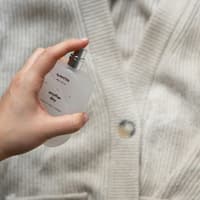 Jemand sprüht ein Parfum auf eine Strickjacke.