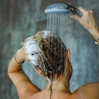 Frau wäscht sich in der Dusche die Haare und braust sie mit Wasser ab.
