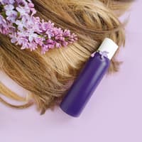 Haare einer Frau liegen mit Orchideen und einer lila Flasche auf einem rosafarbenen Hintergrund.