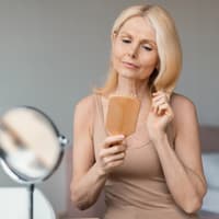 Bei Haarausfall sollten wir laut Expertin täglich Haarewaschen – aus DIESEM Grund. Reife Frau bürstet Haare kritisch