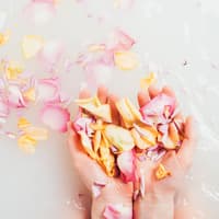 Diese blumigen Drogerie-Duschgele duften nach Frühling. Frau streut Blütenblätter ins Badewasser.