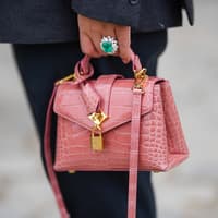 Edelstein-Schmuck in allen möglichen Formen ist wieder im Trend. Eine kleine rosane Tasche wird von einer Hand mit einem Smaragd-Ring gehalten.