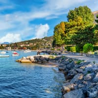 Der Frühling am Gardasee ist die perfekte Reisezeit. Der Gardasee mit Booten auf dem Wasser und Bergen im Hintergrund.