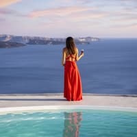 Dieses elegante Maxikleid von H&M versetzt uns sofort in Luxus-Urlaubsstimmung. Frau steht in rotem Kleid am Pool und blickt aufs Meer.