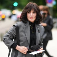 Frau mit dunklem Longbob und Pony trägt eine schwarze Bluse und einen grauen Blazer.