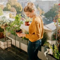 Frau steht auf einem Balkon und hält Pflanzen in der Hand.