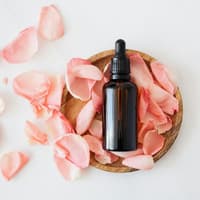 Self Tan Drops sind perfekt für die Anwendung im Gesicht. Eine Flasche mit Pipette liegt in einer Holzschale mit Rosenblättern.