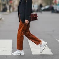 Frau mit Blazer trägt eine rötliche Hose und weiße Sneaker.