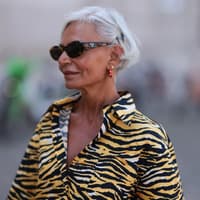 Welches Make-up bei heißem Wetter eine gute Wahl ist, kann eine wichtige Frage am Morgen sein. Frau mit grauen kurzen Haaren, einer Sonnenbrille und einem getigerten Oberteil guckt zur Seite.