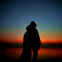 Ein Paar steht Rücken an Rücken vor dem Nachthimmel.