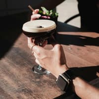 Jemand hält seine Hand an ein Espresso Martini Glas auf einem Tisch.