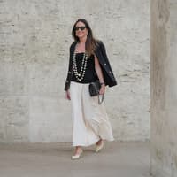 Maxi-Röcke im Boho-Stil liegen wieder total im Trend. Frau trägt einen weißen Maxi-Rock im Boho-Stil mit einem schwarzen Top und Blazer und zwei großen Perlenketten.