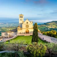 Basilika von Assisi auf einem Hügel mit viel Grünfläche drum herum.