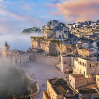 Matera sieht im Morgennebel richtig mystisch aus. Ein Blick auf Matera mit vielen beigefarbenen Häusern und Nebel drum herum.