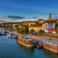 Ein Blick über den Hafen von Belgrad mit Schiffen im Wasser und Häusern an Land, die von der Sonne beleuchtet werden.