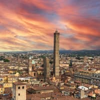Bologna ist eine Stadt in Italien, die mit Gastronomie, Historie und Charme überzeugt. Ein Blick über die Dächer von Bologna bei einem rötlichen Himmel.