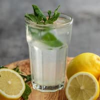 Ein großes Glas mit Wasser und frischer Minze drin, drum herum liegen aufgeschnittene Zitronen.