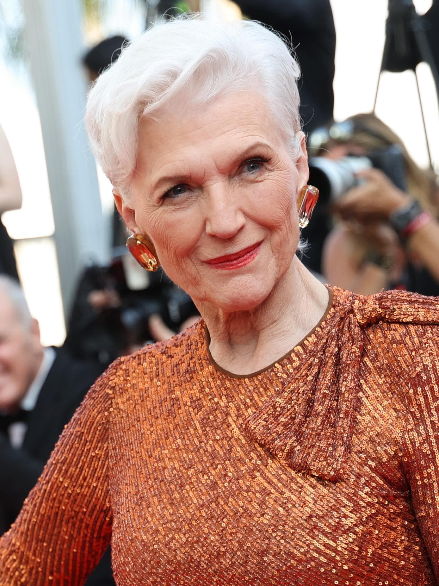 Maye Musk auf den Cammes Filmfestspielen mit grau weißen Haaren und bronzefarbenen Kleid kurze Haare