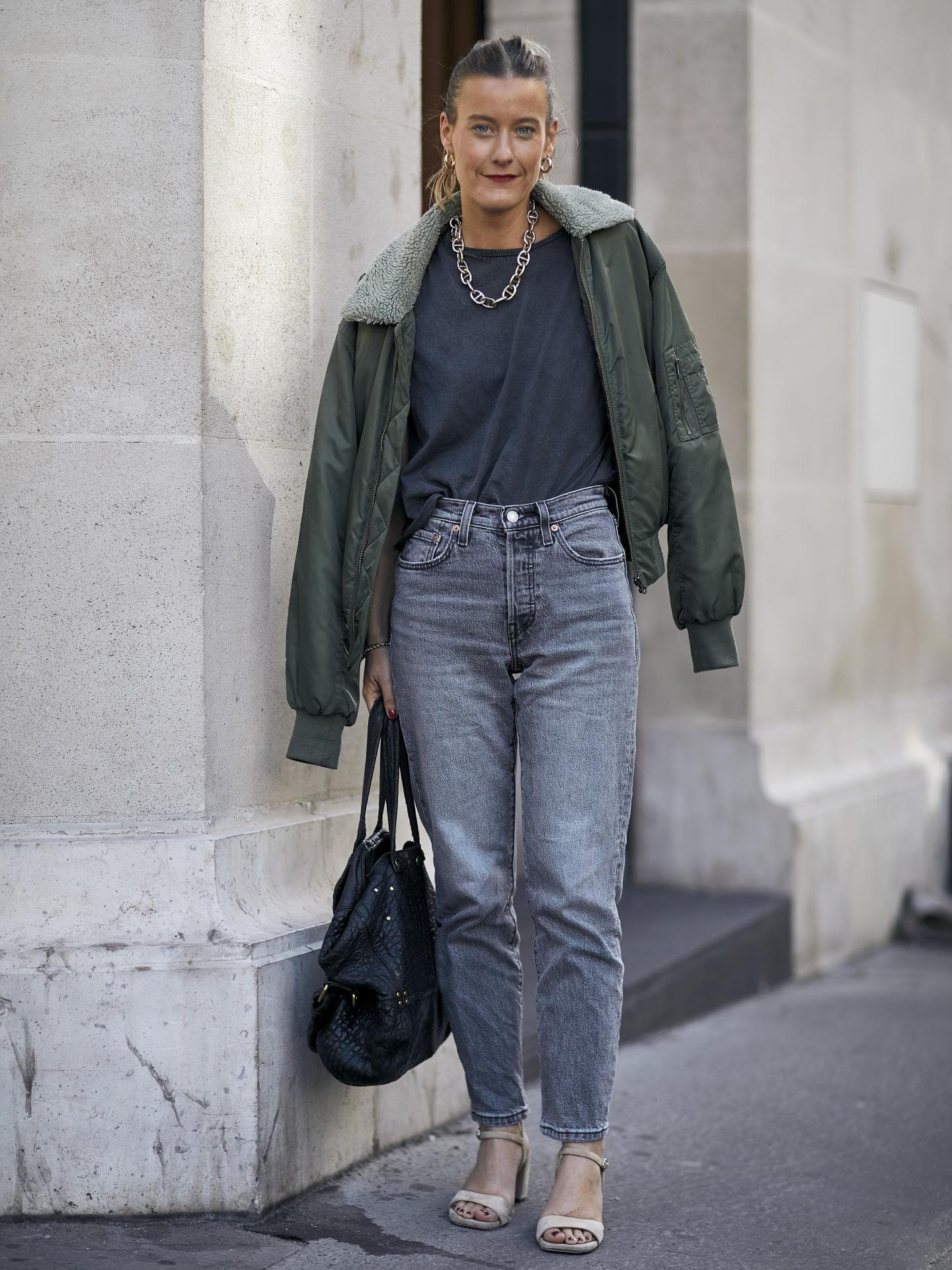Frau trägt auf Paris Fashion Week graue Jeans, dunkelgrüne Bomberjacke, T-Shirt und Tasche