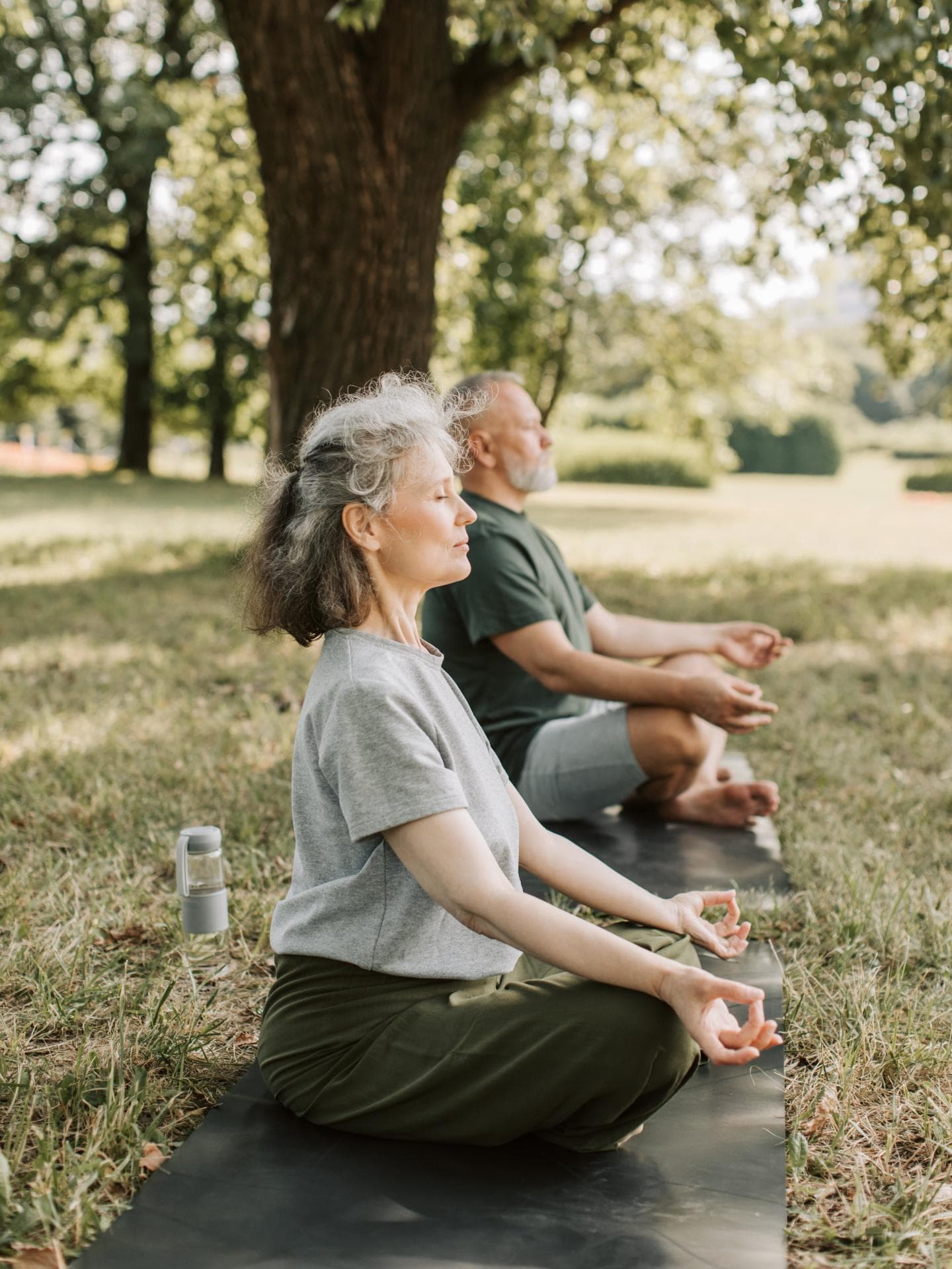 Gesunde Routine tragen zu einer höheren Lebensqualität bei. Älteres Paar macht Yoga auf einer Wiese.