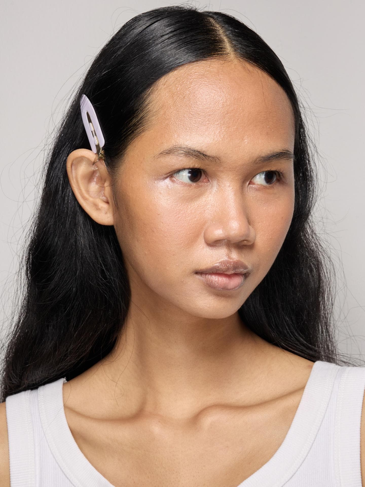 Model mit dunklen Haaren und Haarspange guckt zur Seite.