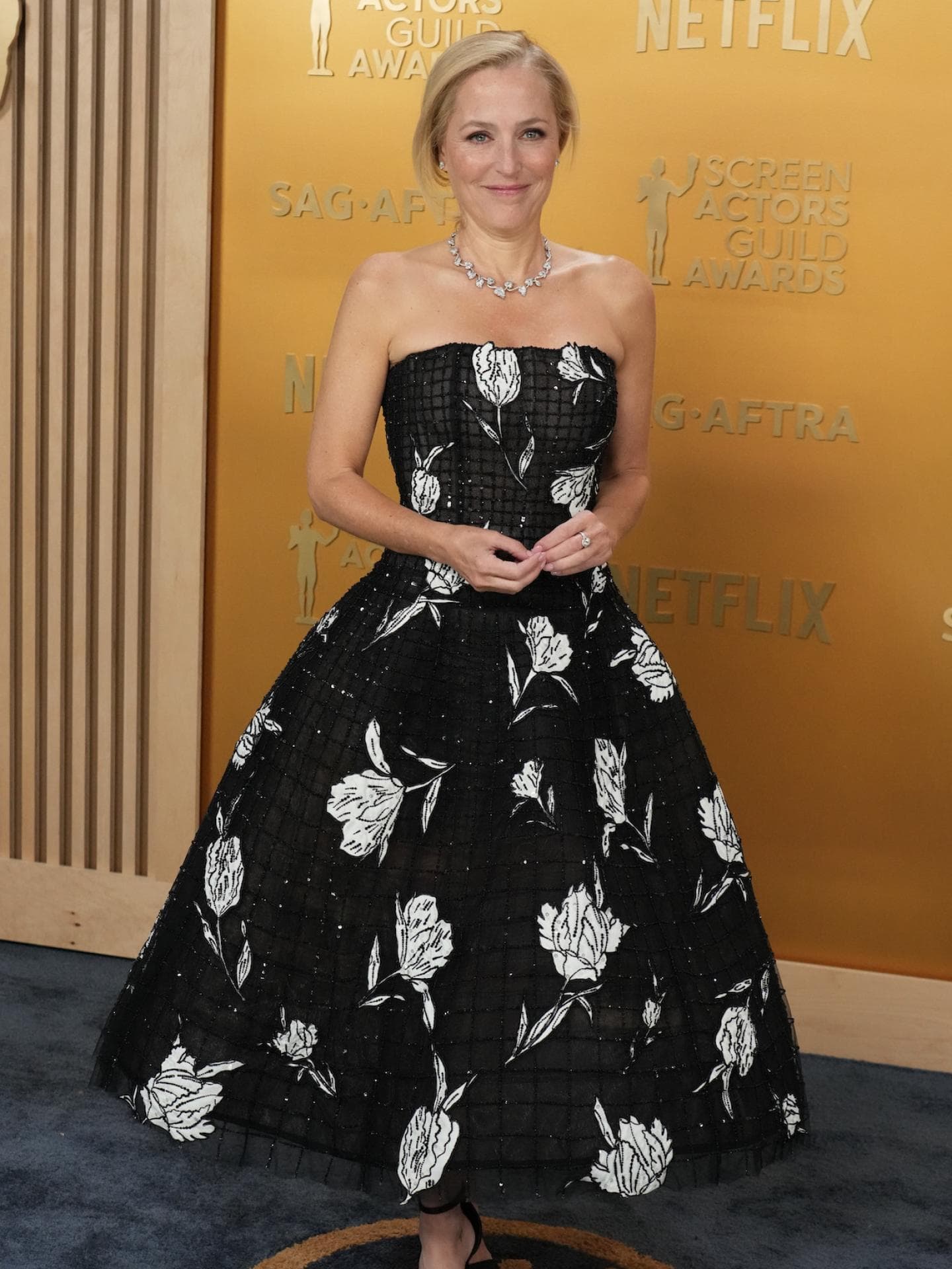 Gillian Anderson in einem schwarzen Kleid mit weißen Blumenmustern.