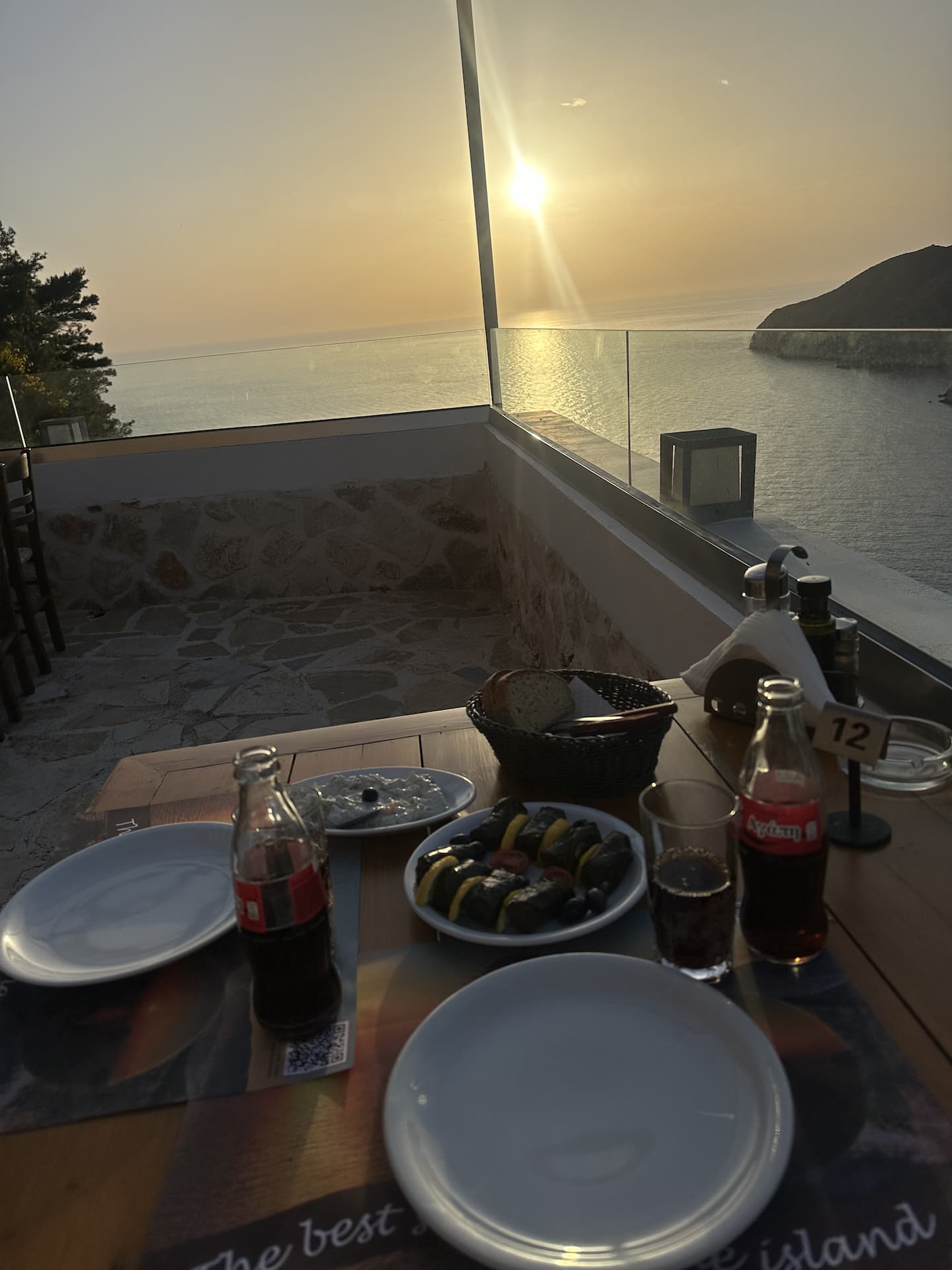 In der Sunset Michalis Taverna kannst du den Sonnenuntergang beobachten. Ein Blick auf einen Tisch mit Essen und Trinken und den Sonnenuntergang über dem Meer im Hintergrund.
