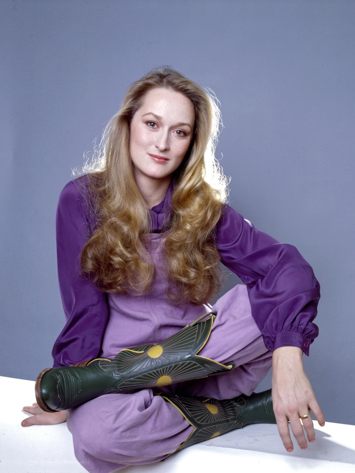 Meryl Streep mit einer lilafarbenen Bluse und Hose sowie Cowboystiefeln und langen blonden Haaren.