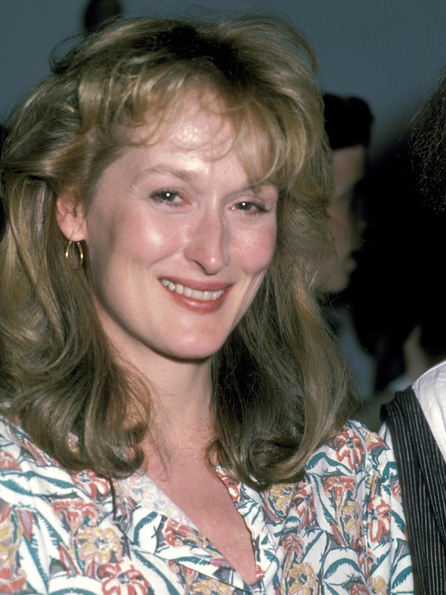 Meryl Streep mit einer Föhnfrisur, kleine Creolen und einem geblümten Oberteil.