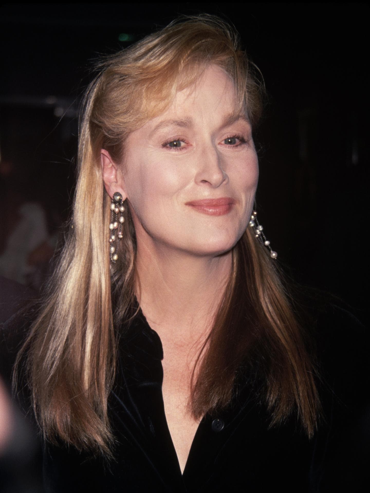 Meryl Streep mit blonden langen Haaren und langen Ohrringen mit Perlen und einer schwarzen Bluse.