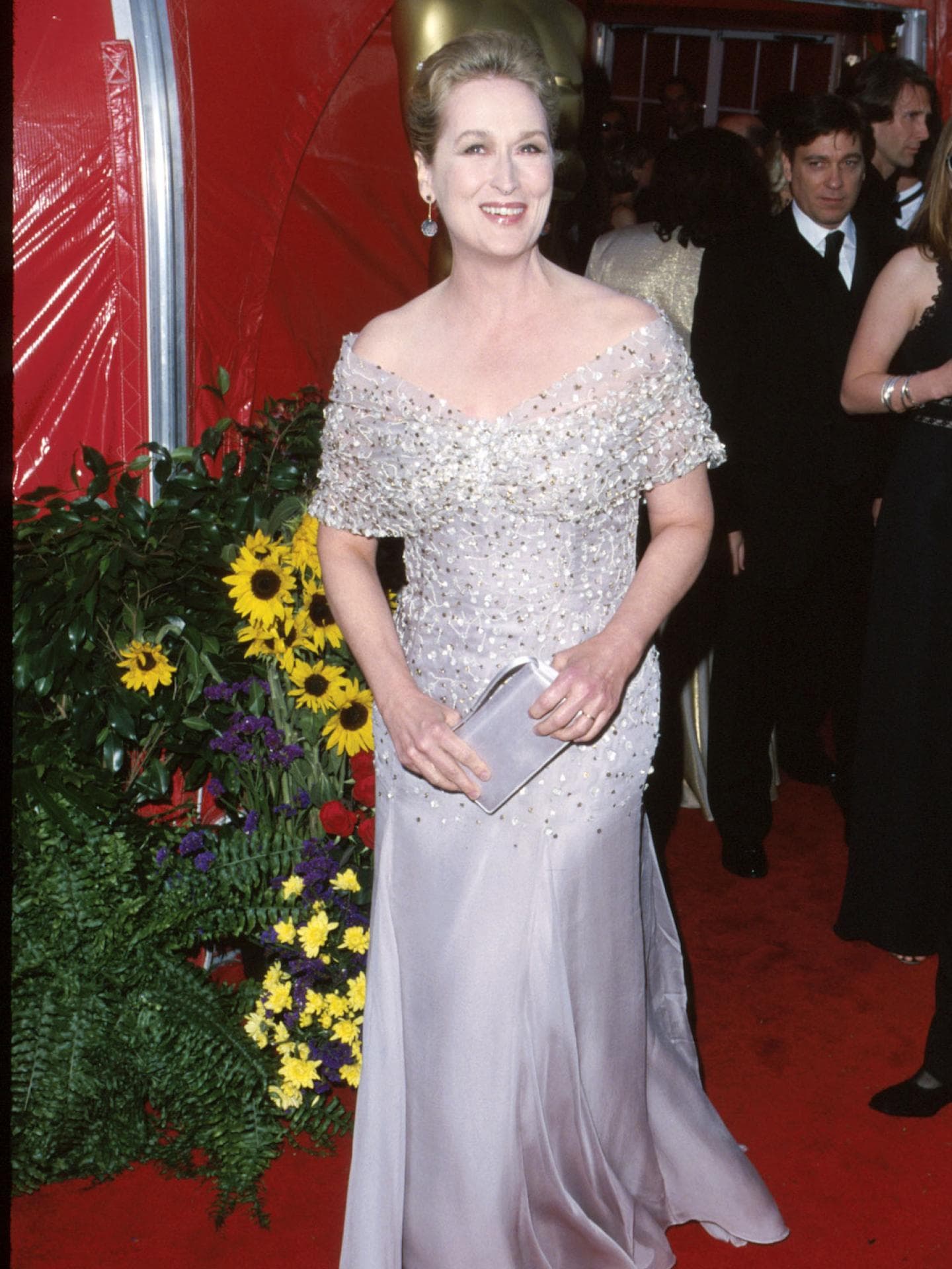 Meryl Streep mit einem langen, glitzernden und schulterfreien Abendkleid auf dem roten Teppich mit Menschen im Hintergrund.