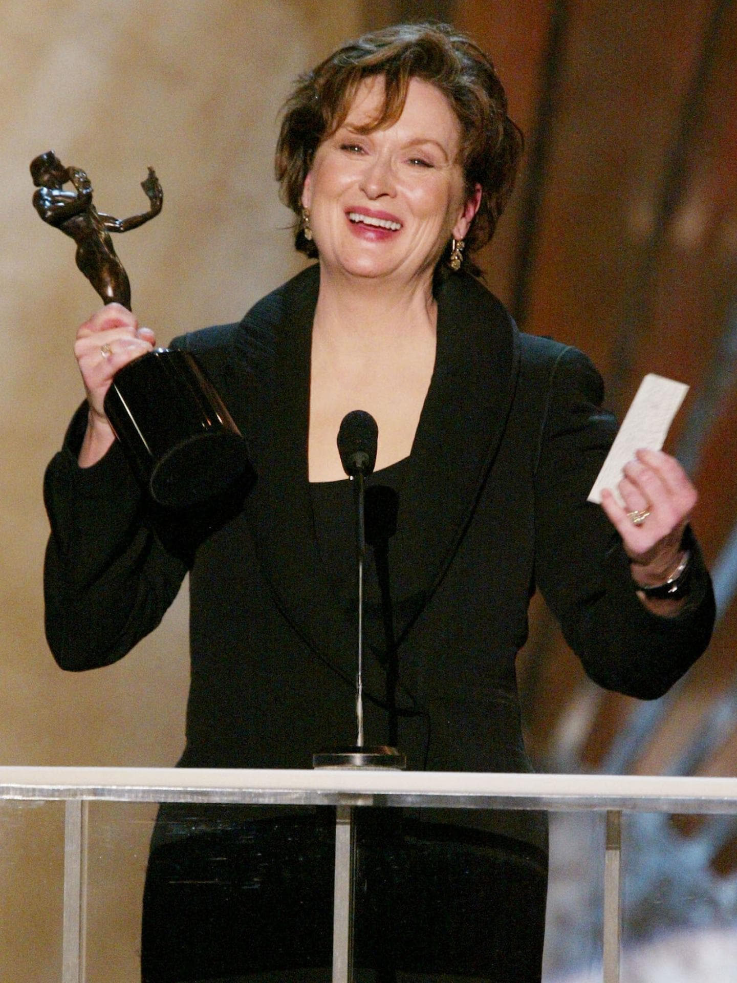 Meryl Streep steht mit einer Preisfigur in der Hand an einem Mikrofon.