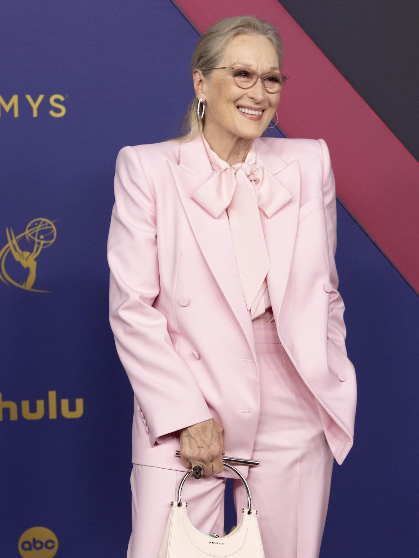 Meryl Streep mit einem rosafarbenen Anzug und einer weißen kleinen Tasche.