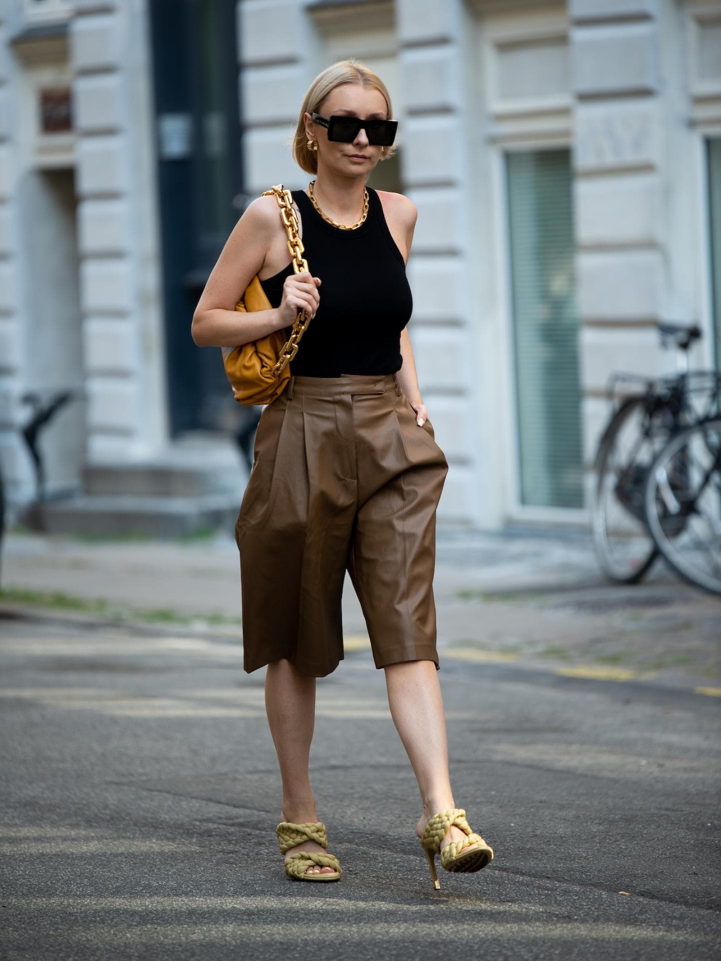 Eine Culotte kann casual mit einem Basic-Top kombiniert werden. Frau mit blonden kurzen Haaren und Sonnenbrille trägt ein schwarzes Top und eine braune Culotte-Hose.