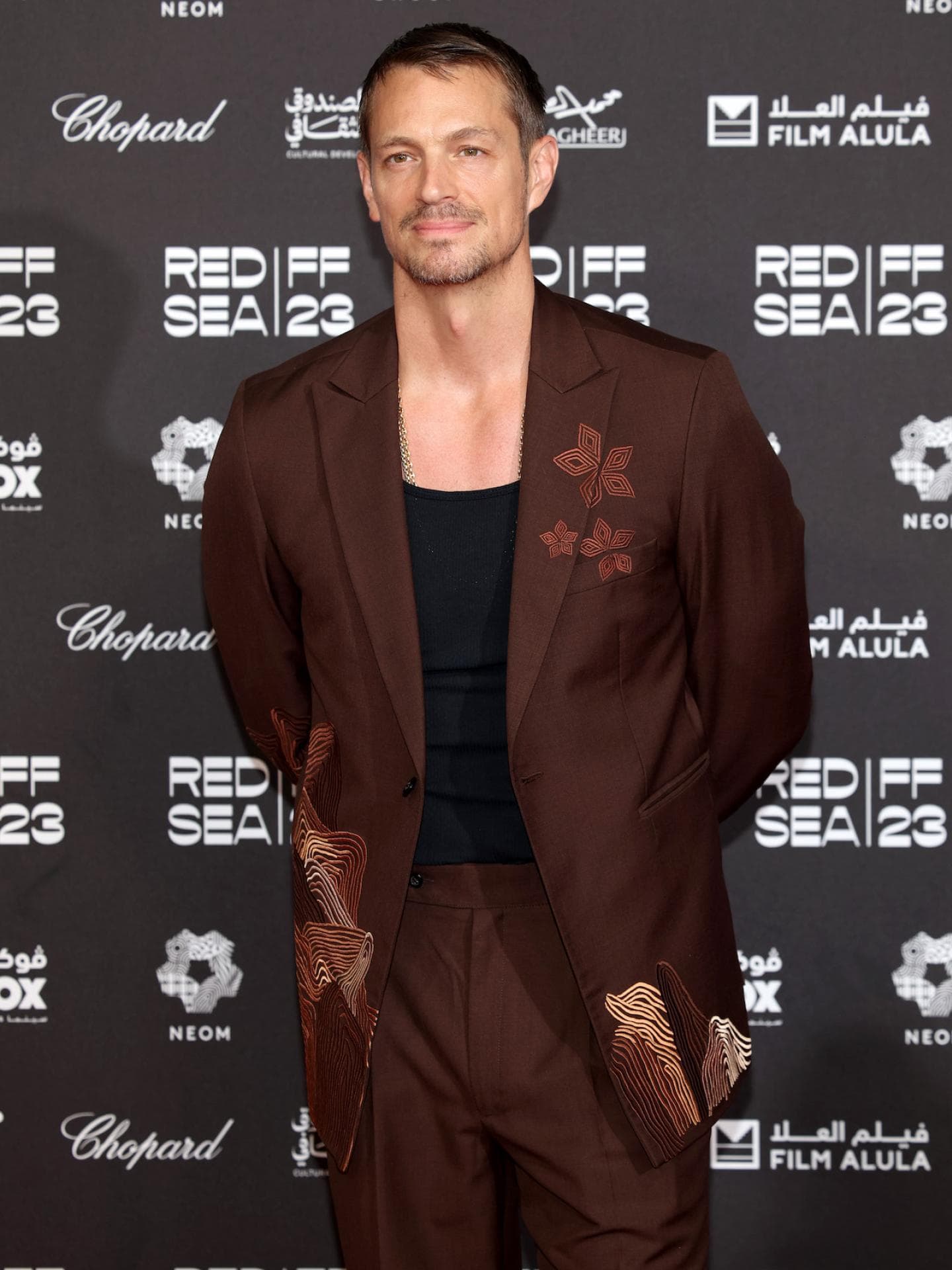 Joel Kinnaman mit einem braunen Anzug und einem schwarzen Shirt darunter auf dem roten Teppich.