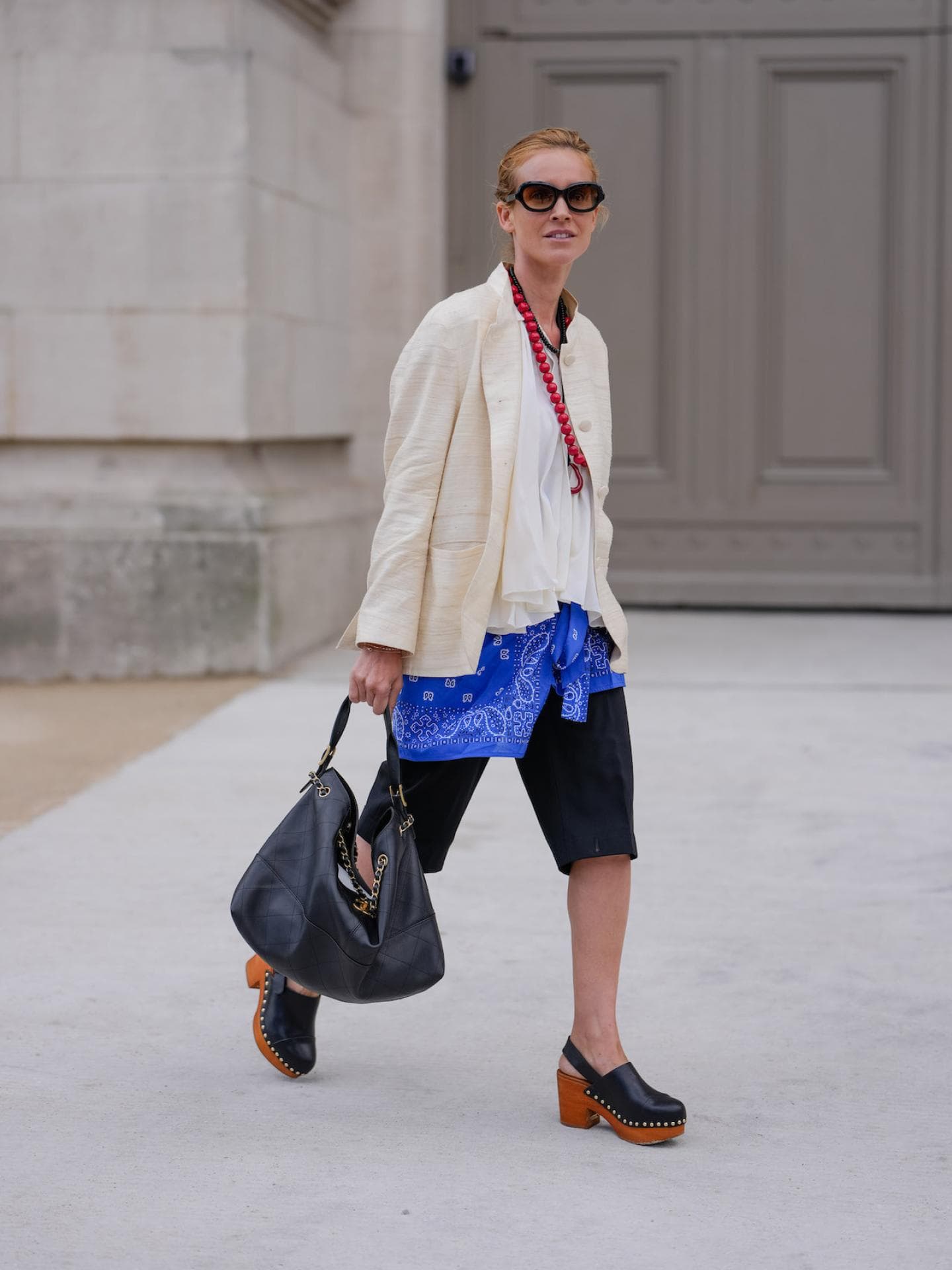 Frau mit beigem Blazer, schwarzen Shorts und Clogs.