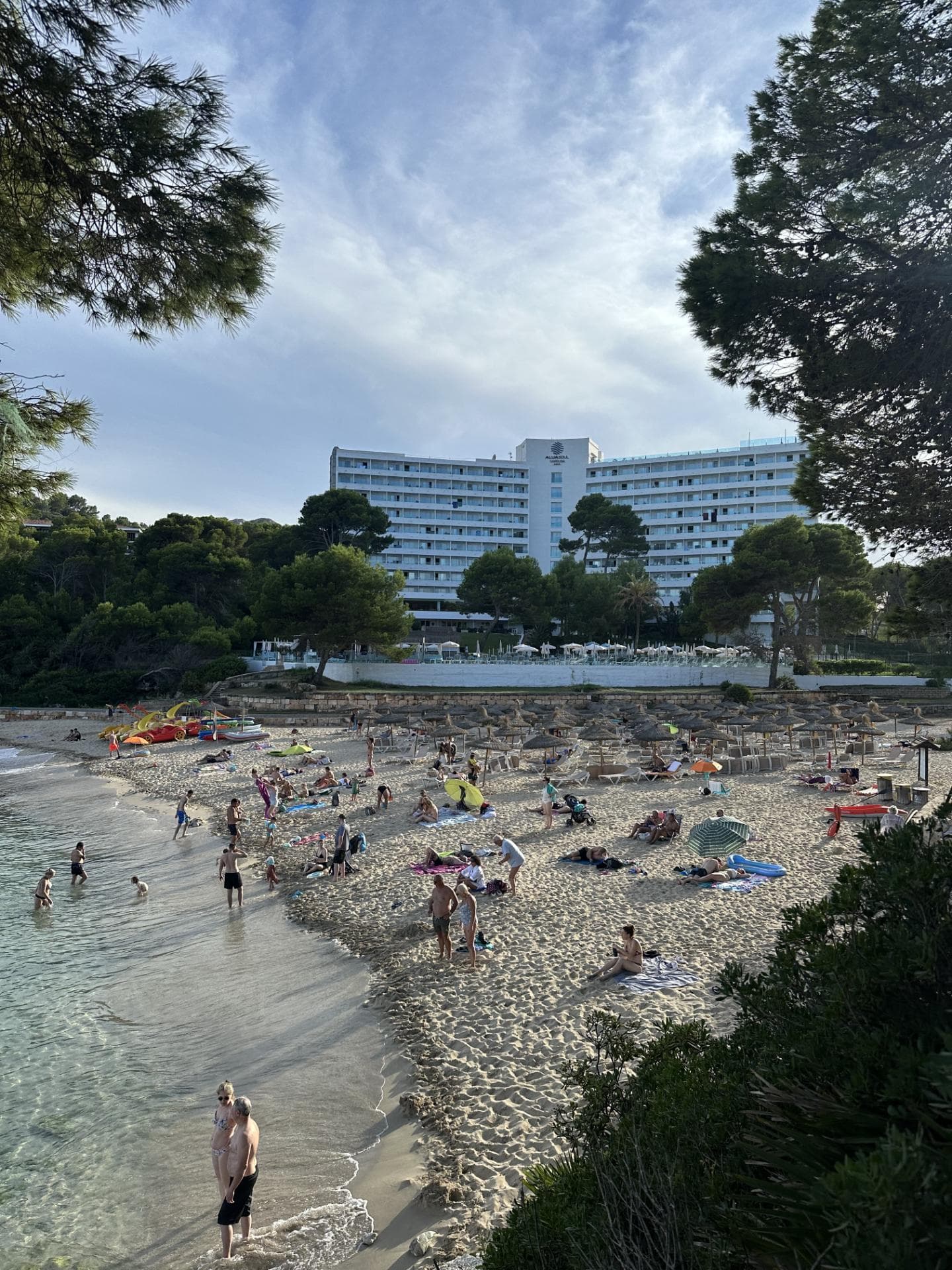 Ein Strand mit Sonnenschirmen, einigen Menschen und einem Hotel im Hintergrund.