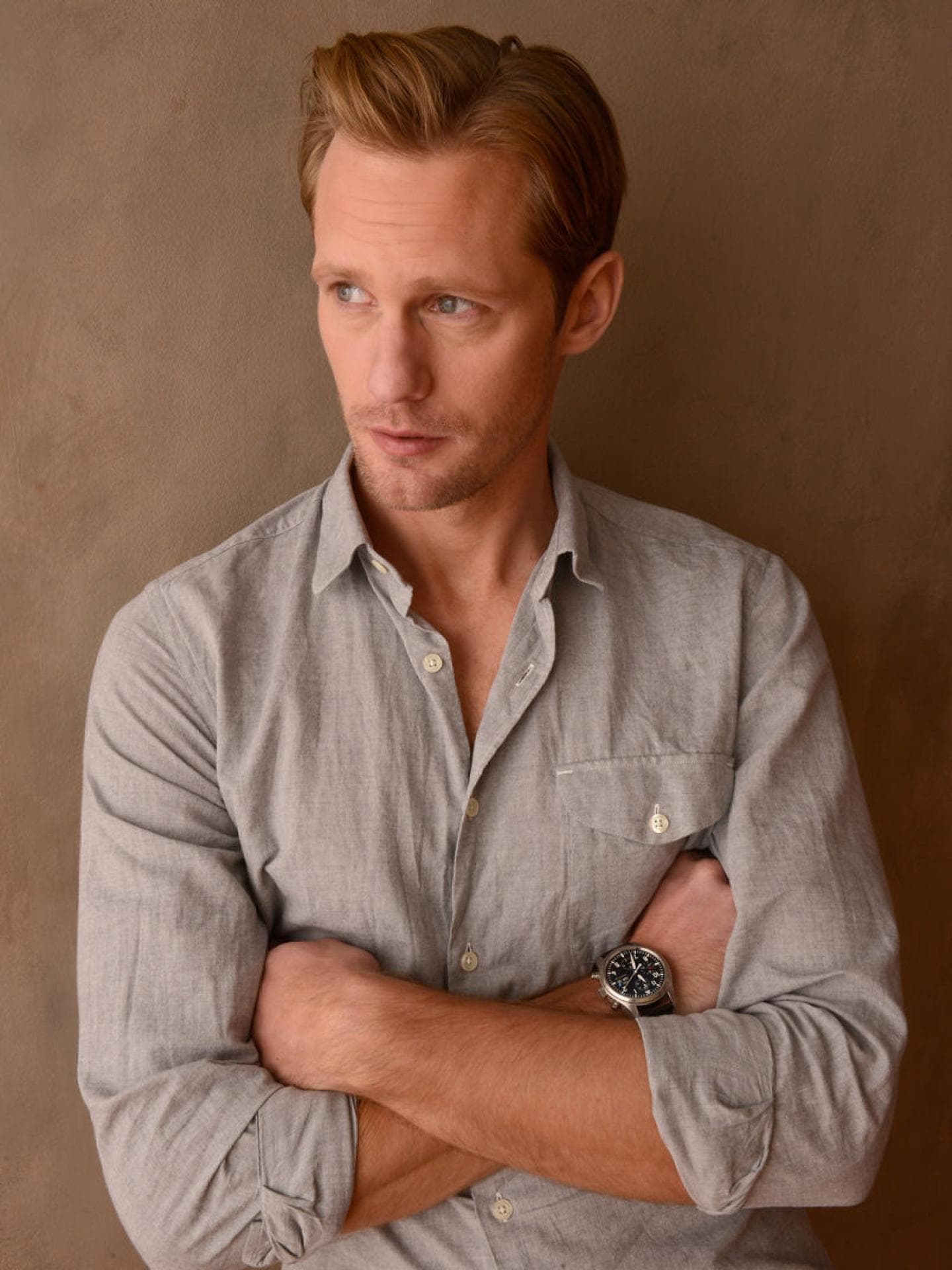 Alexander Skarsgard mit einem hellgrauen Hemd und verschränkten Armen vor der Brust.