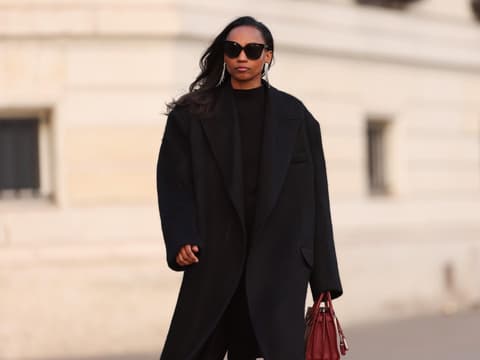 Frau trägt schwarzen Oversize-Mantel und rote Handtasche