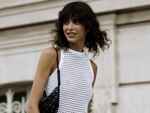 Frau auf Paris Fashion Week trägt weißes Kleid und lockige Haare mit Pony Frau auf Paris Fashion Week trägt weißes Kleid und lockige Haare mit Pony