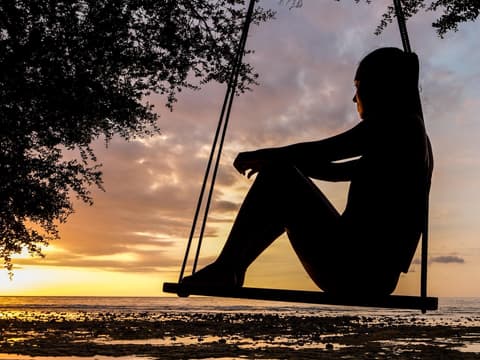 Eine Frau sitzt auf einer Schaukel und blickt in den Sonnenuntergang.