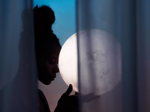 Sternzeichen, die eine Auszeit brauchen Frau mit Dutt hält eine Kugel in der Hand, die aussieht wie der Mond