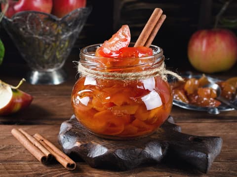 Rezept für eine weihnachtliche Bratapfelmarmelade Bratapfelmarmelade im Glas steht auf einem Holztisch mit Zimtstangen