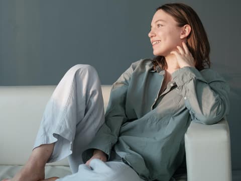 Frau sitzt lächelnd auf dem Sofa.