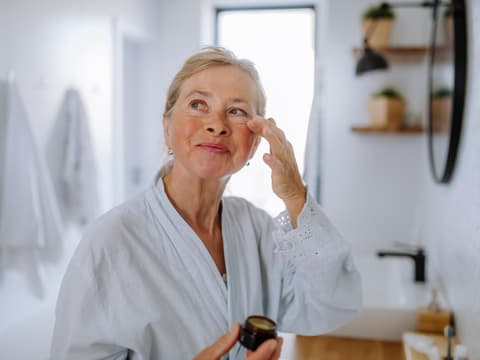 Ältere Frau trägt Augencreme mit Lichtschutzfaktor auf.