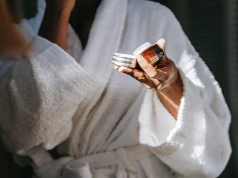 Frau im Bademantel hält eine Cremedose in der Hand. 