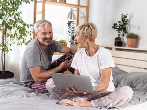 Älteres Pärchen sitzt im Bett am Laptop.