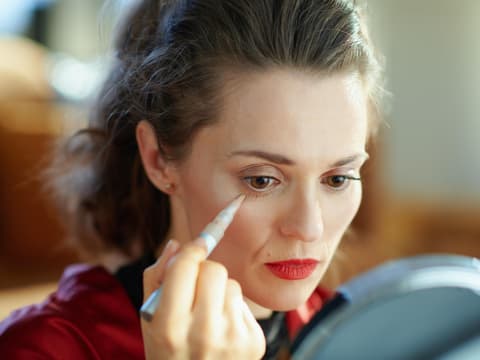Frau sitzt vor dem Spiegel und deckt ihre Augenringe mit Concealer ab.