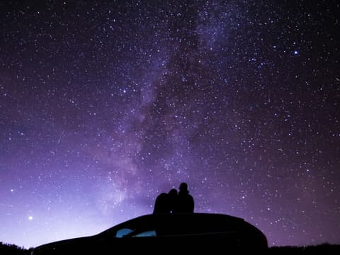 Pärchen sitzt auf Autodach und schaut in den Sternenhimmel