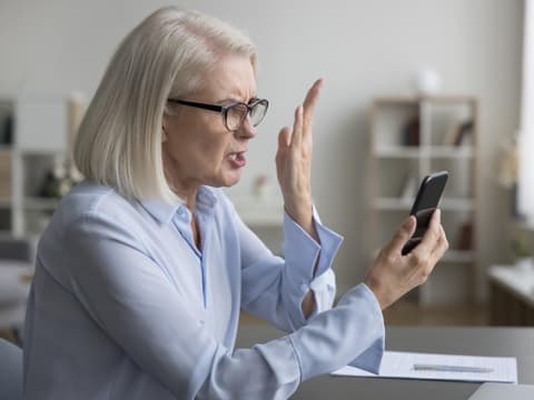 Frau liest etwas auf dem Handy und beschwert sich.